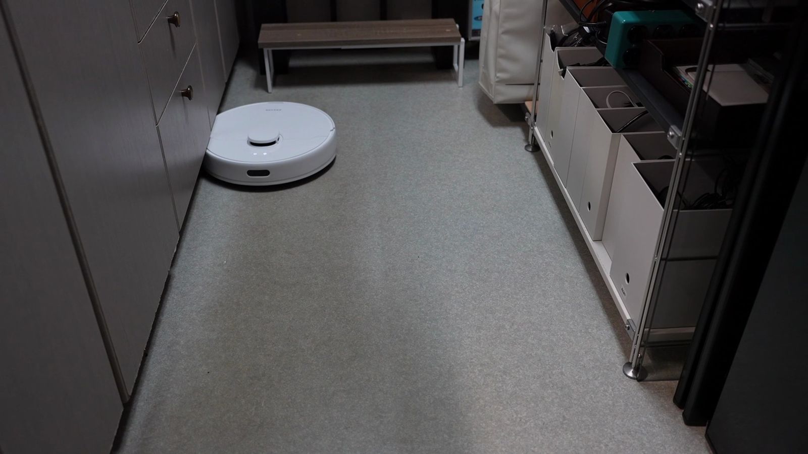 床に物がない部屋を走行するロボット掃除機。壁際の棚に道具が収まっている