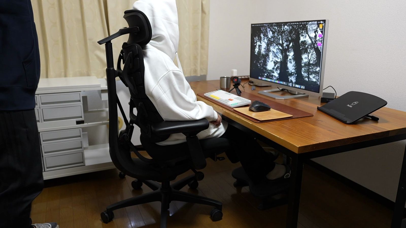木製デスクの下で専用フットレストに足を乗せて座った様子