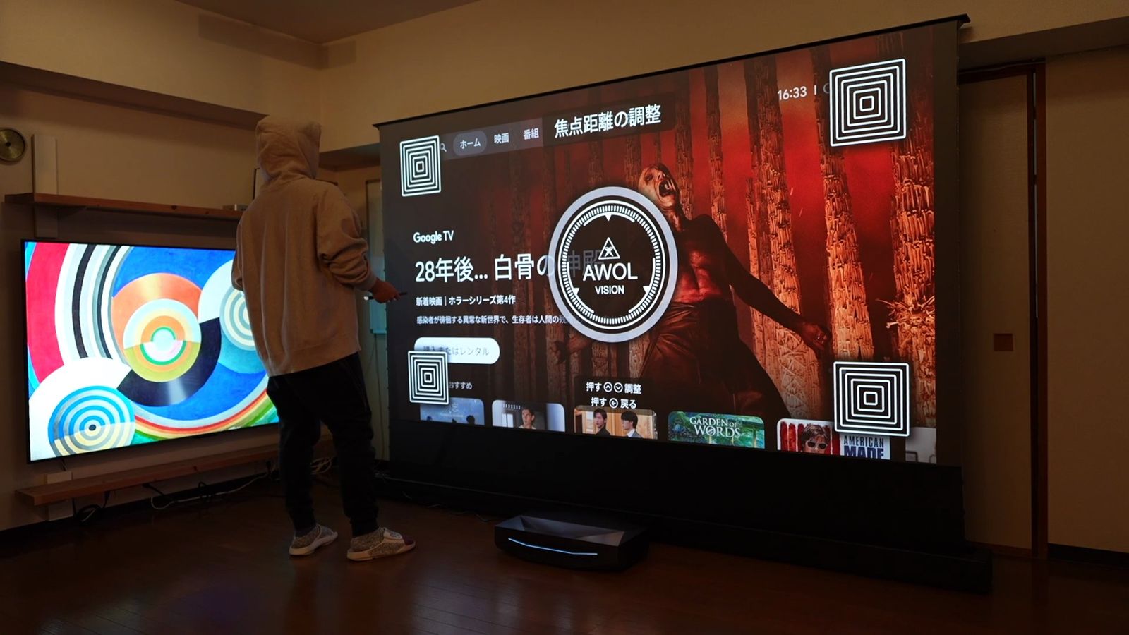 リビングの大画面にGoogle TVの画面とピント調整の図形を投影し、スクリーンの横に人が立っている