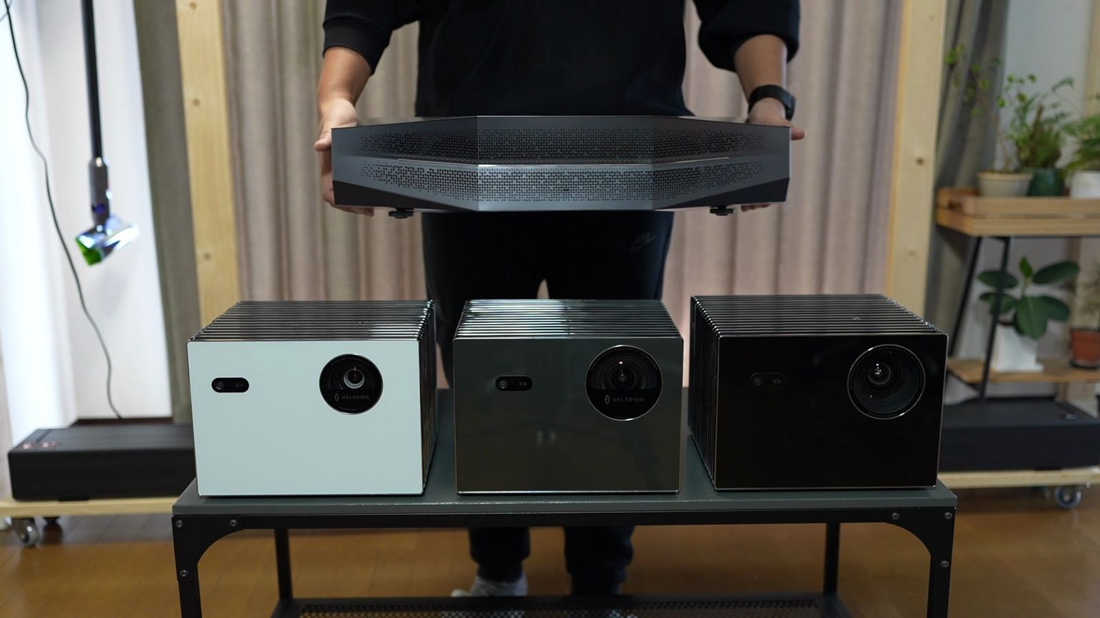 棚に並べたValerionのプロジェクター3台の上で、Aetherion Maxを両手で持っているところ