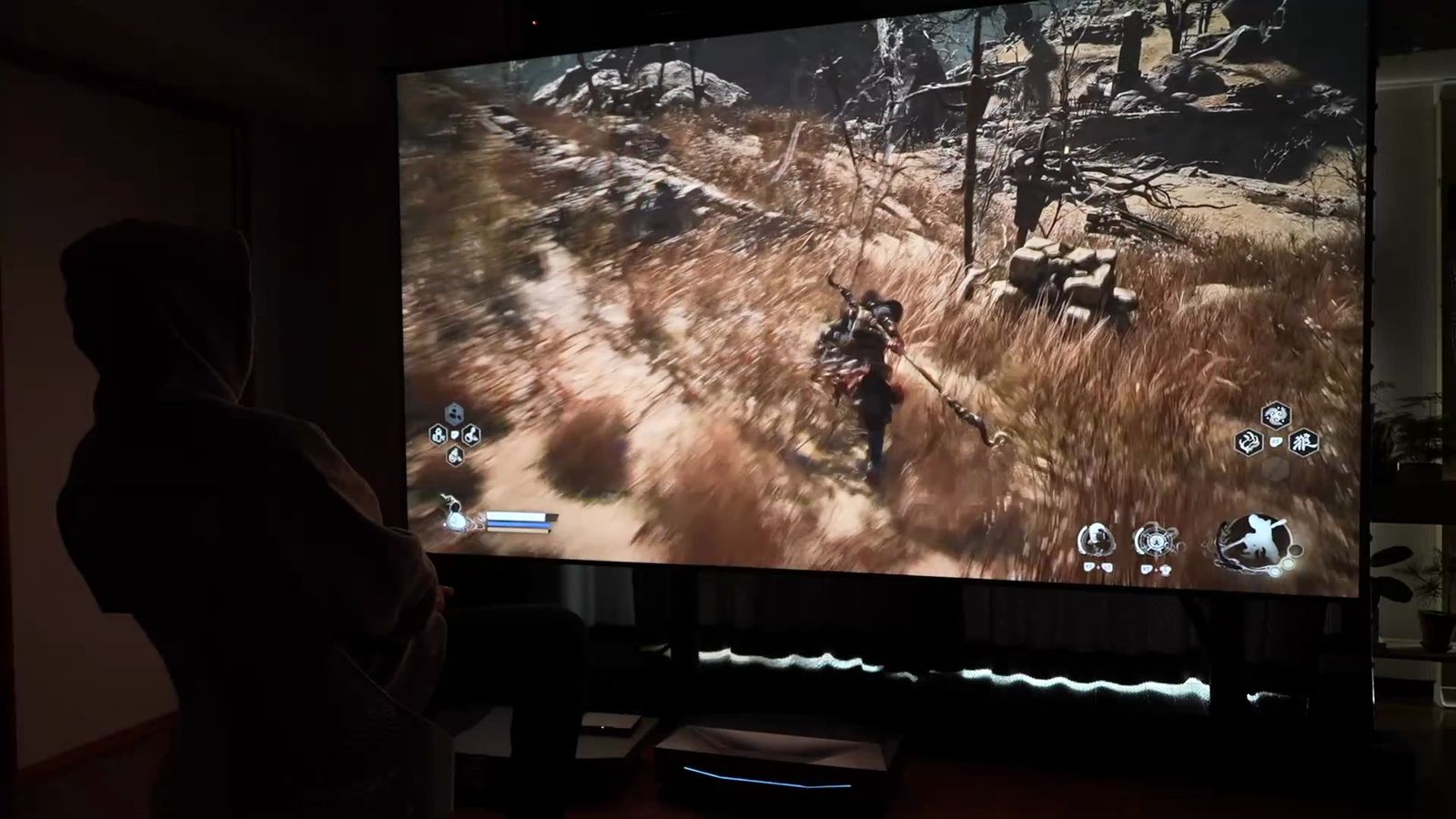 暗い部屋で大画面に投影したアクションゲームと、その前に座る人
