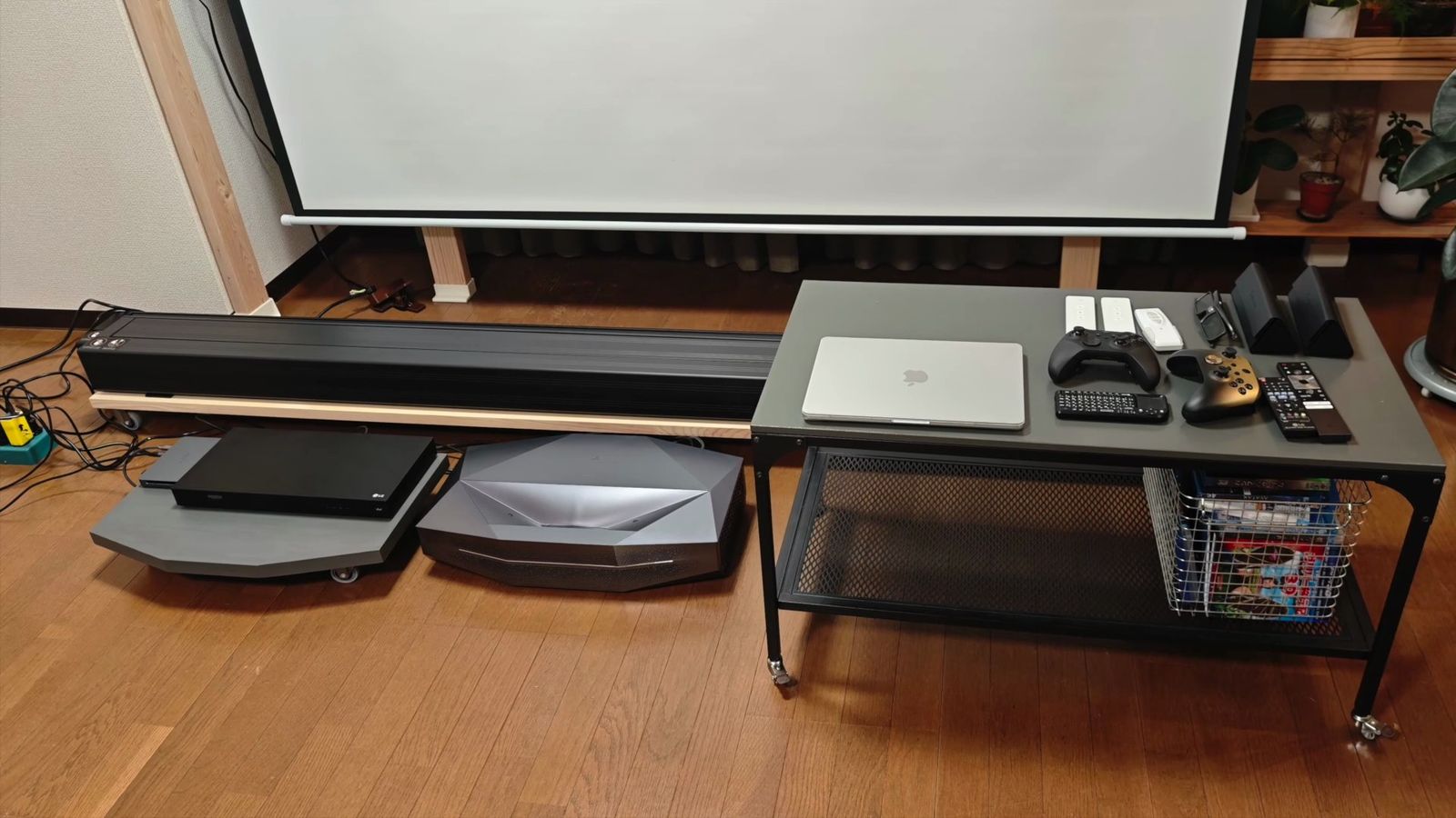スクリーンの手前にサウンドバーと本体を並べ、横のテーブルに機器を置いたところ