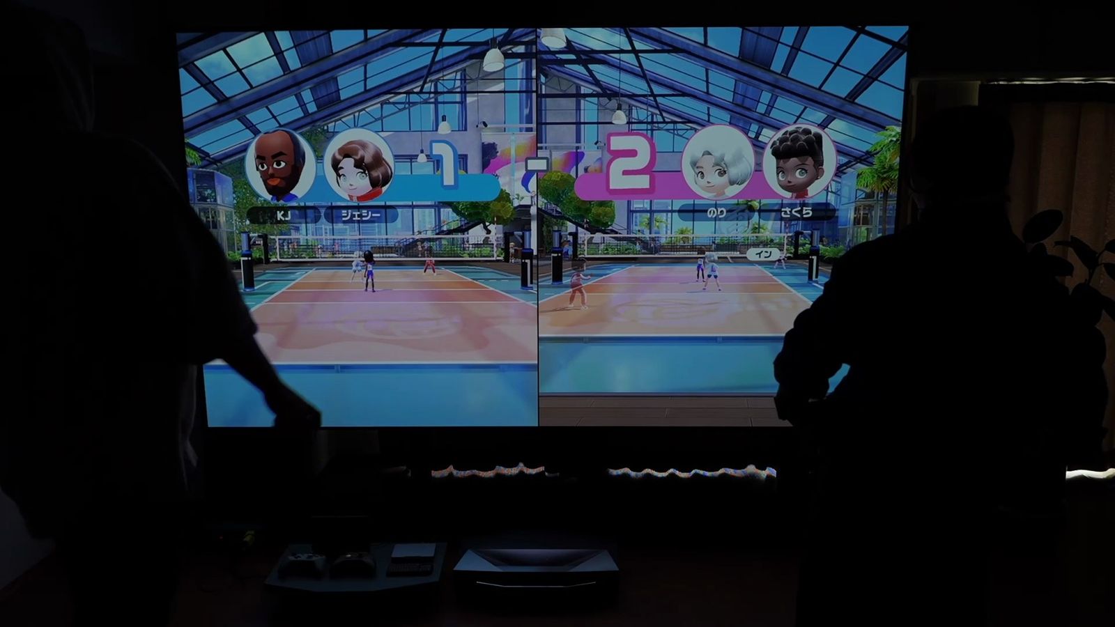 2人がスクリーンの前に立ち、画面を分割してパーティーゲームをしているところ