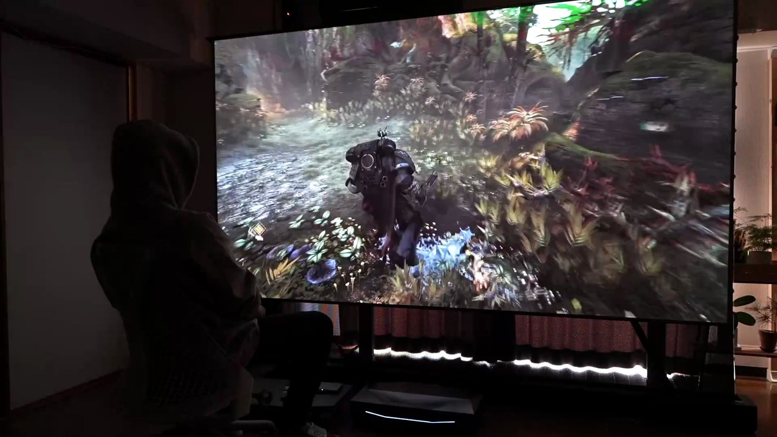 暗い部屋で大画面に投影したゲームと、その前に座る人