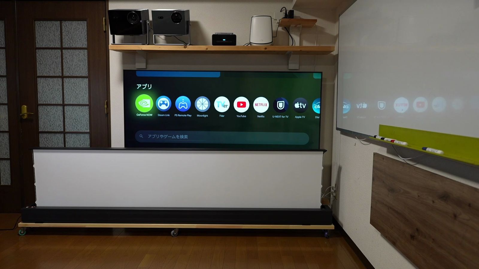 リビングの床置きスクリーンに、Google TVのホーム画面を投影したところ