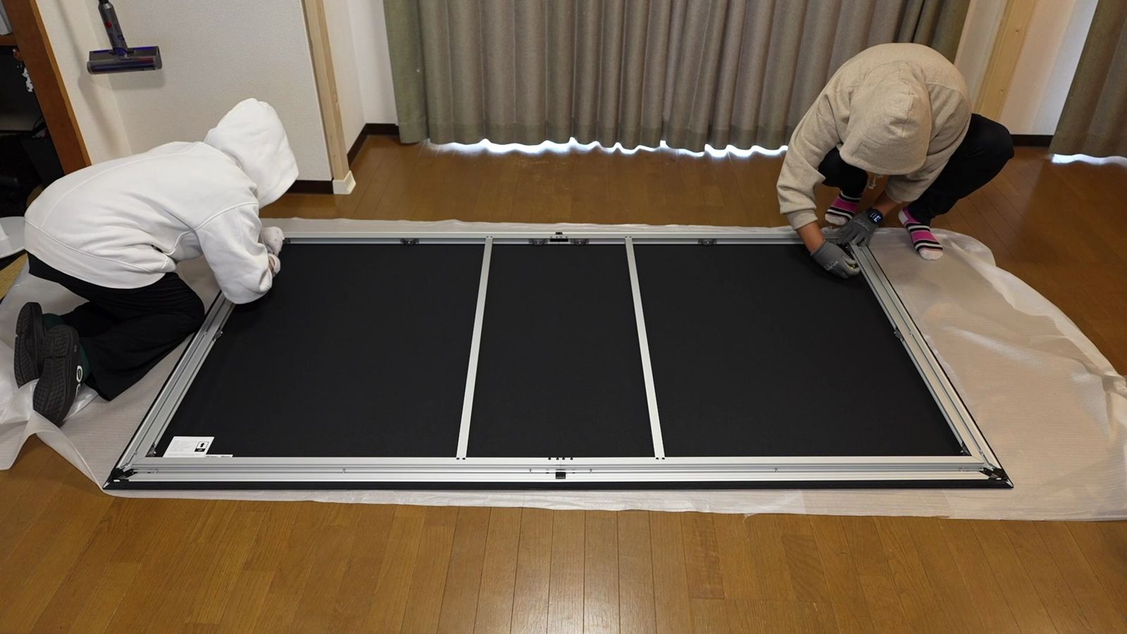 床に置いたフレームの両側で、2人で組み立て作業をしているところ