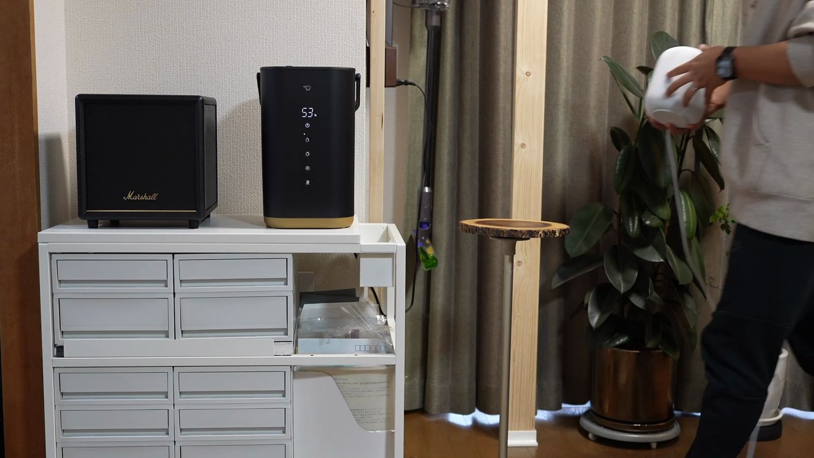 リビングの棚に置いたサブウーファーと、HomePodを手に持つ人