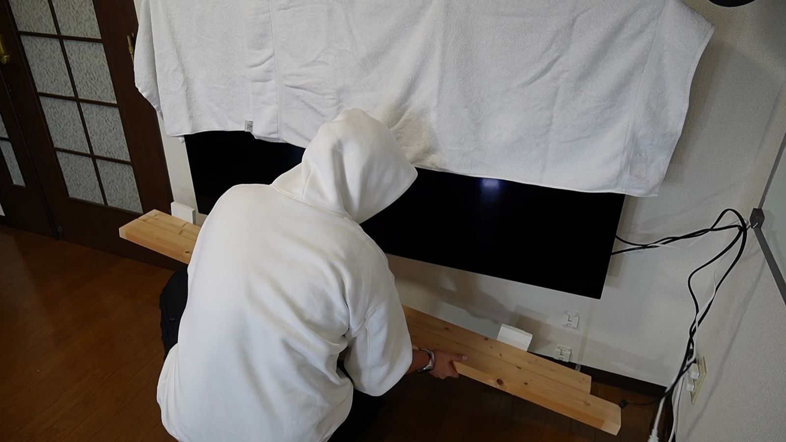 テレビの下の壁に棚板を取り付けているところ