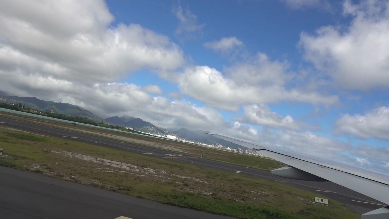飛行機の窓から見た滑走路と主翼、遠くの山
