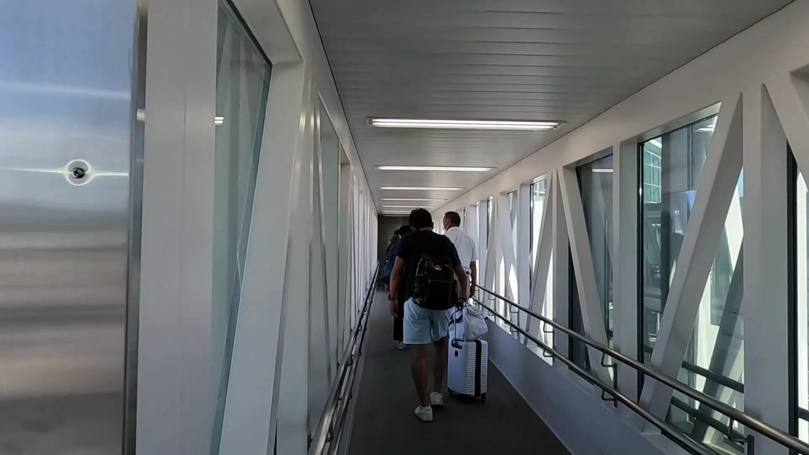 飛行機を降りたあとの搭乗橋の通路を、スーツケースを持った人が歩いている