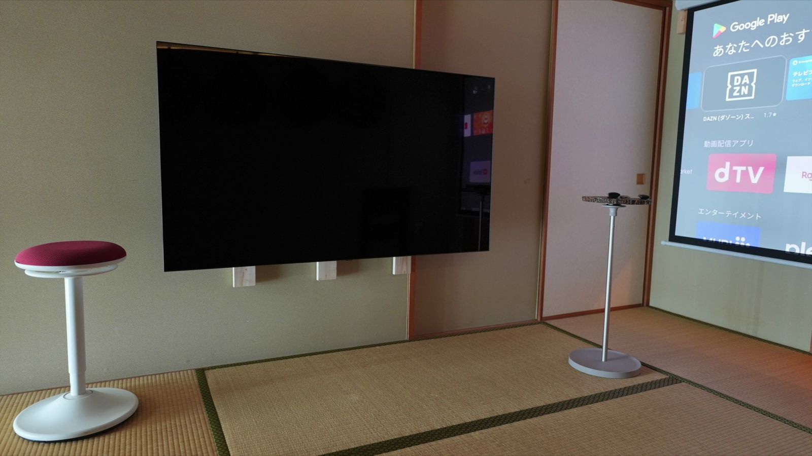 6畳間の壁に横向きで設置した65インチのテレビと、右側のプロジェクターのスクリーン