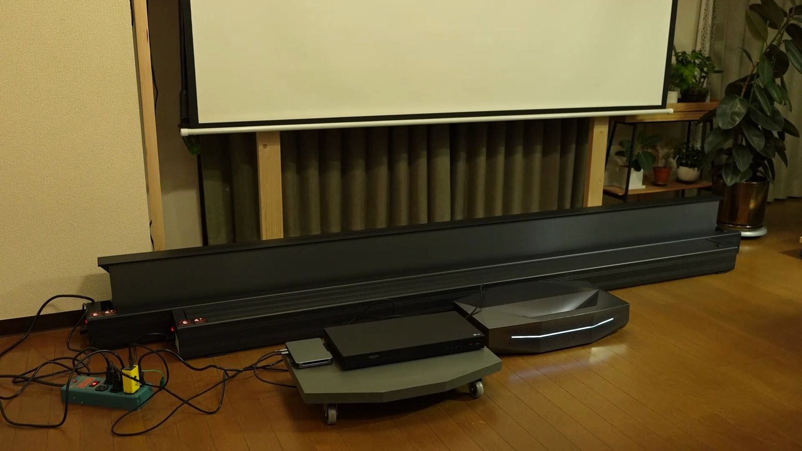 部屋の上部から下げた白い吊り下げスクリーンと、手前の床に置いたポップアップスクリーンの本体