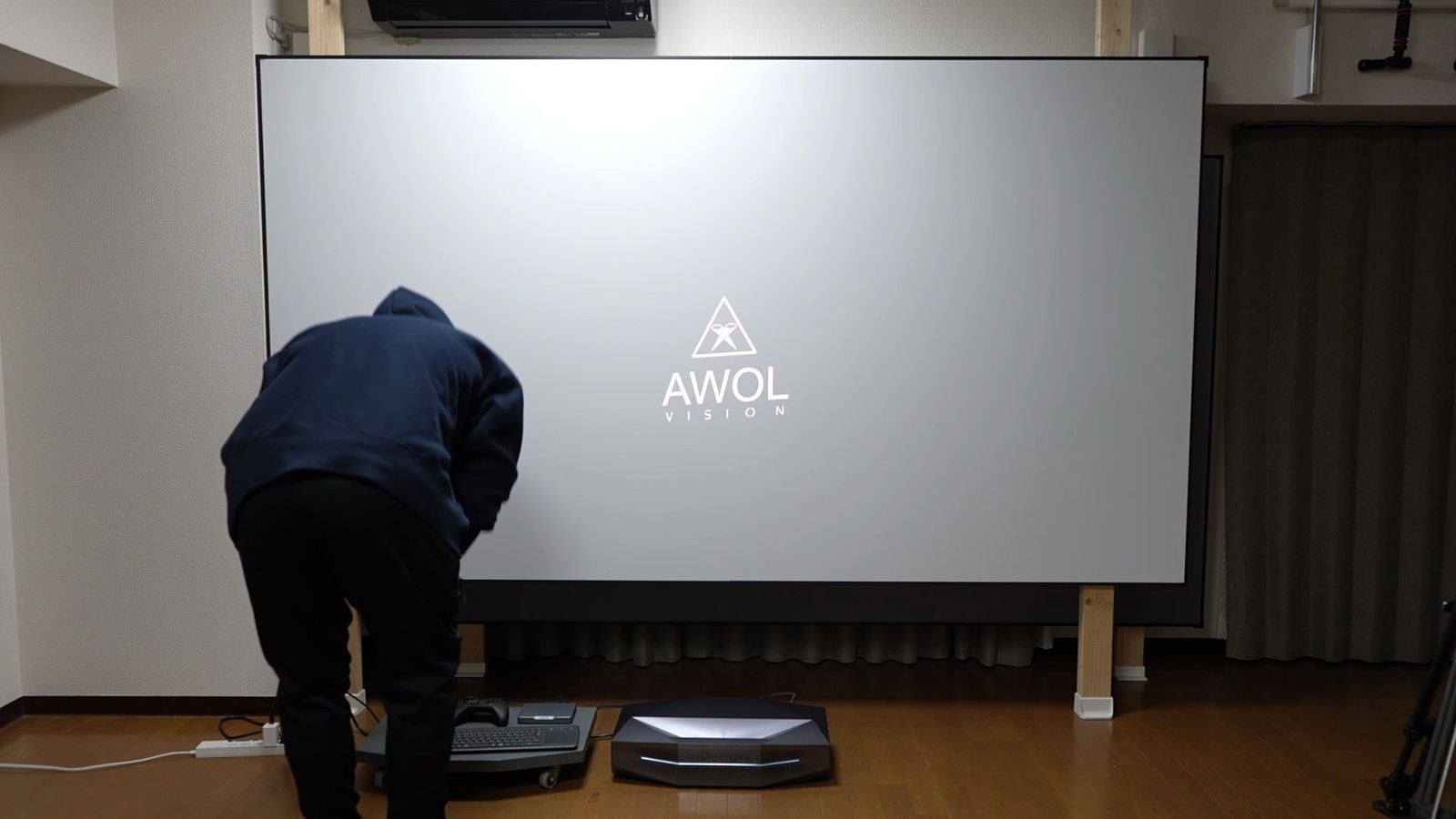 柱に掛けた白いマットスクリーンに投影したAWOLのロゴと、床の本体を調整する人