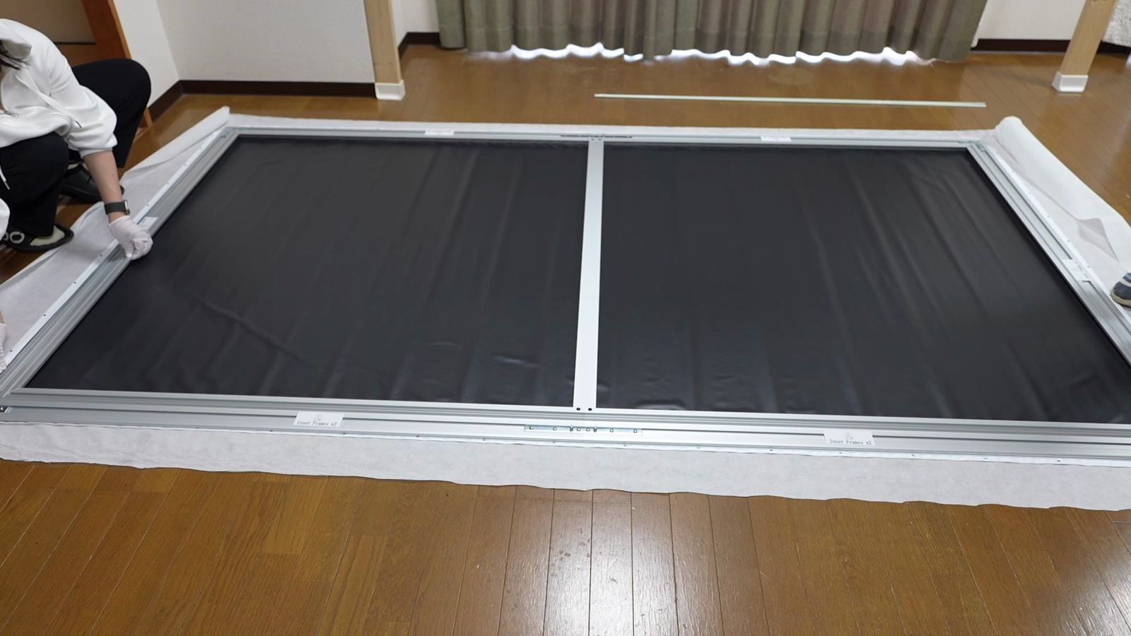 床に置いたスクリーンの裏側。黒い生地の上に銀色のフレームを重ねている