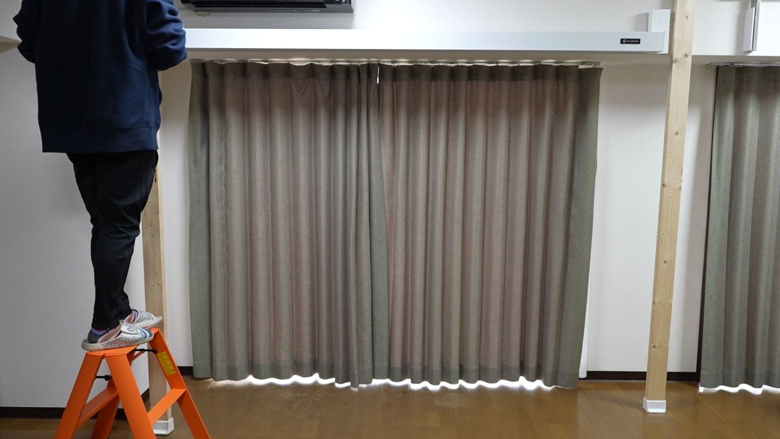 窓の前に立てた木の柱と、脚立に乗って作業する人
