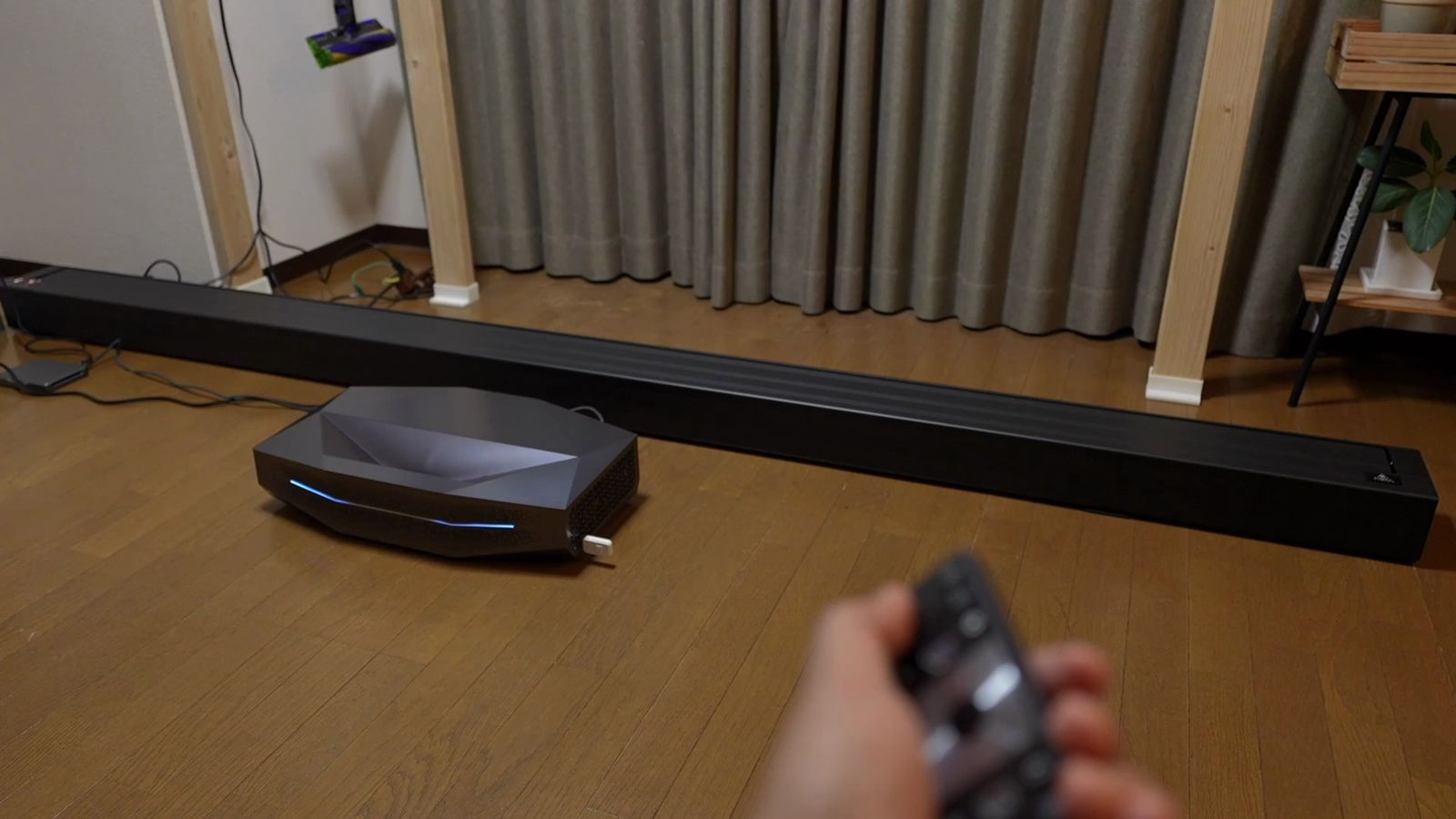 床に置いたポップアップスクリーンの本体とAetherion Maxに、リモコンを向けているところ