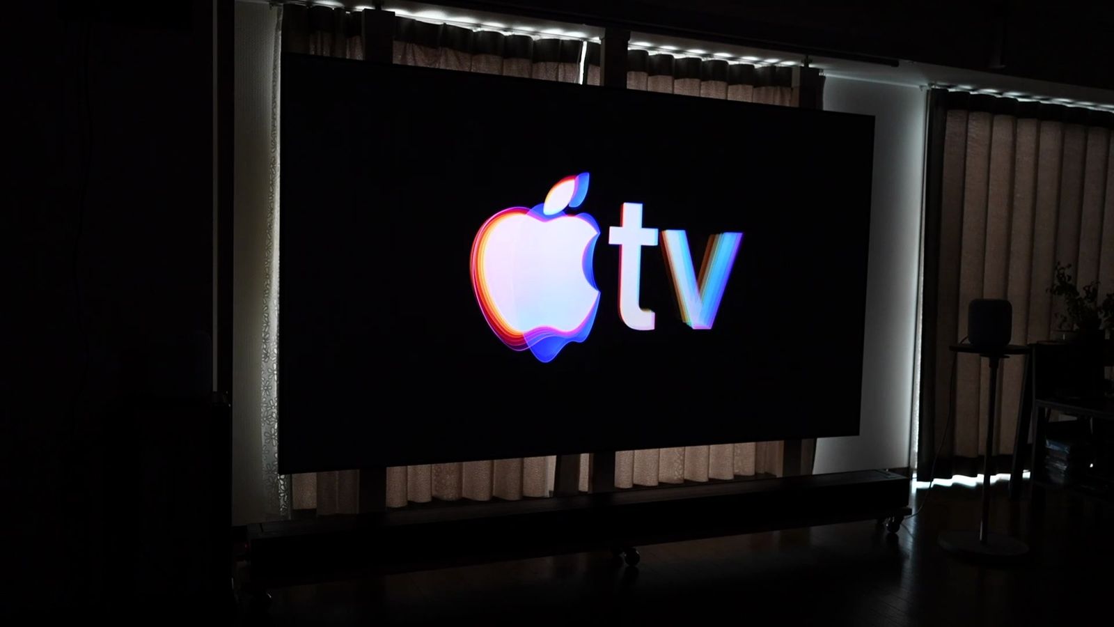 壁掛けの固定フレームのスクリーンに投影したApple TVのロゴ