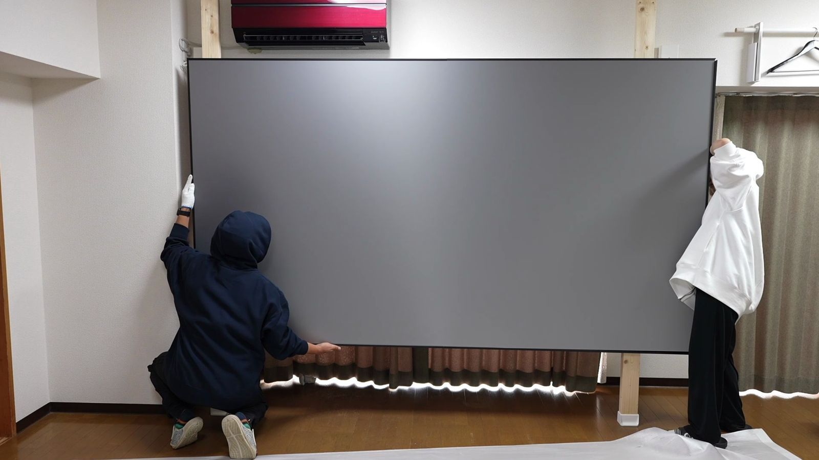 2人で柱にグレーの120インチのスクリーンを掛けているところ