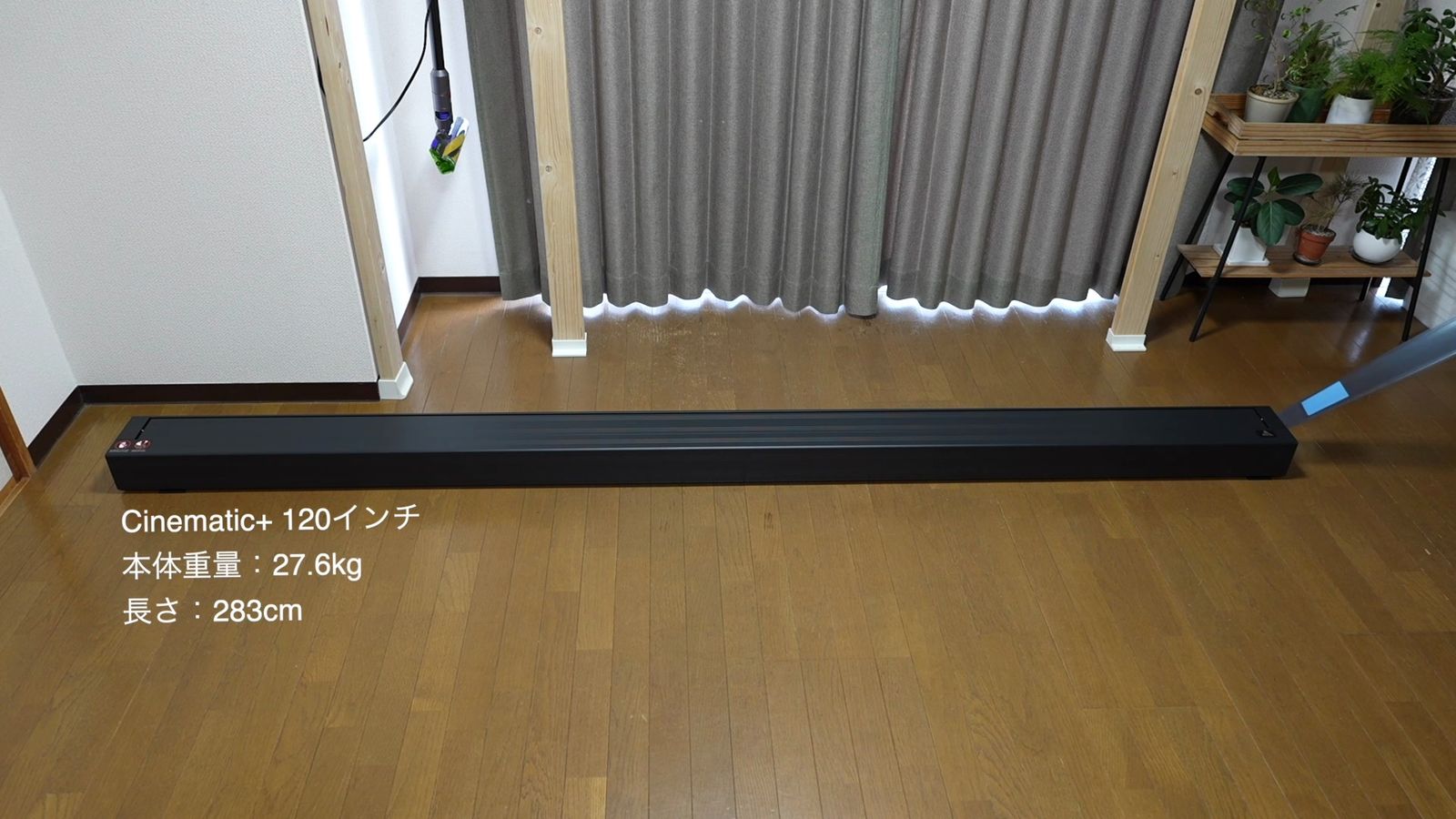 床に置いたポップアップスクリーンの本体(Cinematic+ 120インチ・本体重量27.6kg・長さ283cmの文字入り)